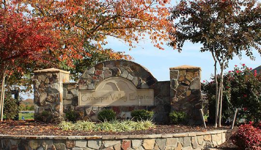 Stone sign reading "Catharpin Valley Estates" flanked by shrubs and trees with fall foliage.